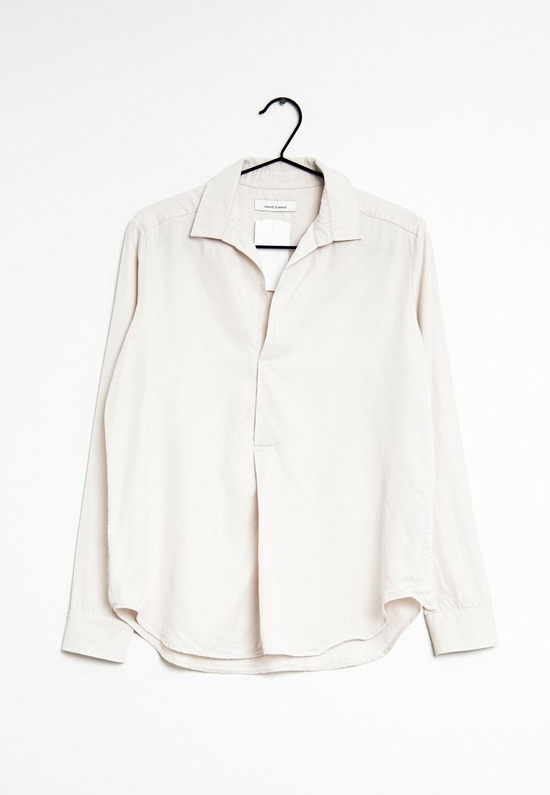 Chemise beige clair à manches longues boutons sur un cintre noir contre un fond blanc.