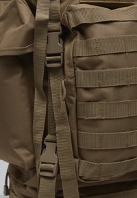 Section de sac à dos tactique marron avec plusieurs sangles horizontales en sangle et deux boucles en plastique à libération rapide sur des sangles réglables.