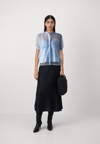 Light blue sheer blouse with button closure and two chest pockets, paired with a black satin maxi skirt and black handbag.