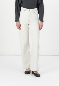 Hvide højtaljede jeans med vide ben, med kontrastsyning og lommer; sat sammen med en grå langærmet top og sorte flade sko.