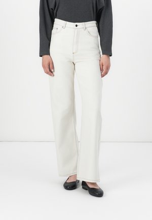 Hvide højtaljede jeans med vide ben, med kontrastsyning og lommer; sat sammen med en grå langærmet top og sorte flade sko.