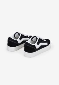 Zapatillas de ante negras con suelas y detalles de goma blanca. Presentan un destacado diseño en forma de ola blanca y un cierre clásico con cordones.
