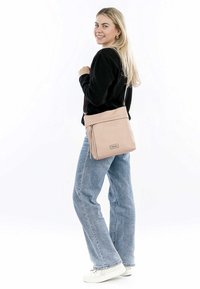 Sac à épaule rose clair en matériau doux, comprenant une poche zippée, une sangle ajustable et un design minimaliste.
