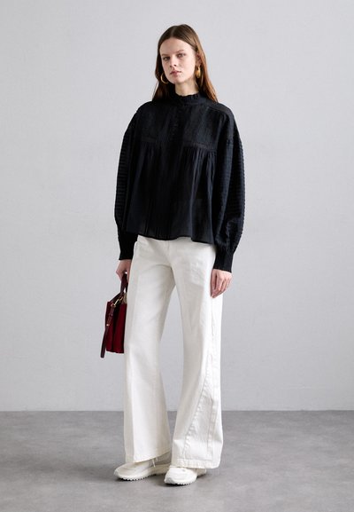 Black long-sleeve blouse with puffed sleeves and textured detailing, paired with white wide-leg pants and a small red handbag. White sneakers.
