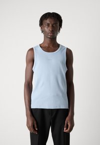 Débardeur côtelé bleu clair avec un col rond, arborant un branding minimaliste. Assorti à un pantalon noir, mettant en avant une silhouette ajustée.