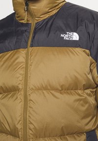 Giacca imbottita marrone e nera con chiusura a zip, caratterizzata da un motivo a scacchi, colletto alto e logo sul lato sinistro superiore.