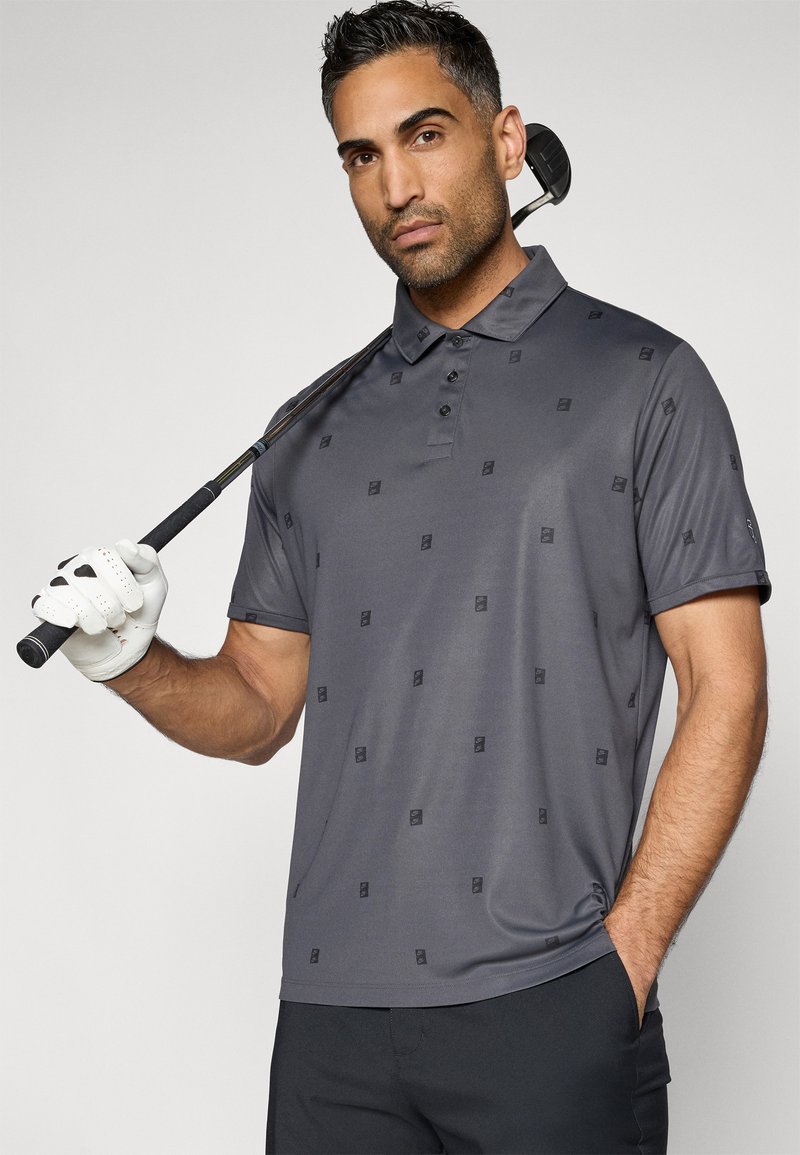 Graues Polohemd mit einem dezenten Muster, glatter Textur und einer Knopfleiste mit drei Knöpfen. Das Modell hält einen Golfschläger und trägt einen Golfhandschuh.