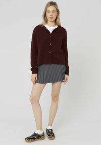 Cardigan bourgogne avec des boutons, porté sur un t-shirt blanc. Assorti à une jupe plissée grise et des baskets imprimé léopard noir et beige.