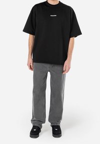 Černé oversized tričko s krátkým rukávem a bílým logem "PEGADOR"; zkombinováno se šedými rovnými džíny a černými teniskami.