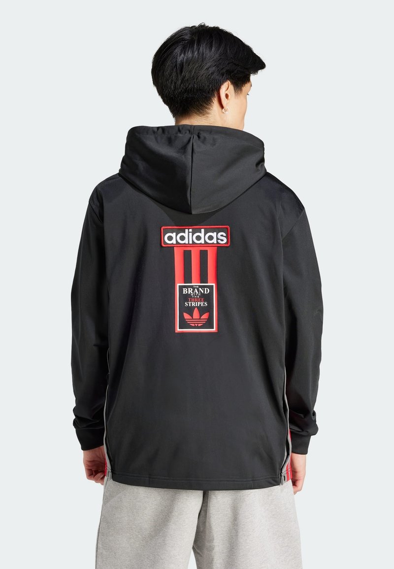 Svart huva jacka med röda detaljer, med en stor Adidas-logotyp och en rektangulär grafik på baksidan, tillverkad av lätt material.