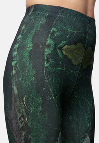 Hoge taille legging in donkergroen met een textuur, abstracte bladdessin en contrasterende gouden accenten, gemaakt van rekbaar materiaal.