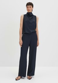 Navy mouwloos top met hoge hals, gecombineerd met loszittende navy broek. Stof lijkt glad met een minimalistisch ontwerp en geen zichtbare patronen.