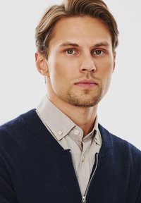 Marynarski sweter na zamek błyskawiczny noszony na jasnoszarym koszuli zapinanej na guziki; gładka tekstura, casualowy design z prążkowanymi mankietami i detalami kołnierza.