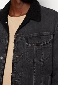 Svart denimjacka med en fluffig svart krage, framfickor och silverfärgade knappar. Texturerat tyg med fransiga nederkanter.