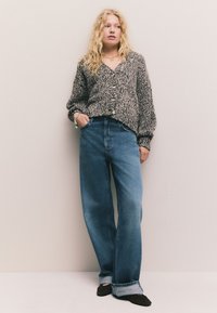 Adīts pelēks un melns kardigans ar pogām, kombinēts ar gaišziliem džinsiem ar augstu jostasvietu un plašām kāju daļām. Gluda tekstūra ar brīvu piegriezumu.