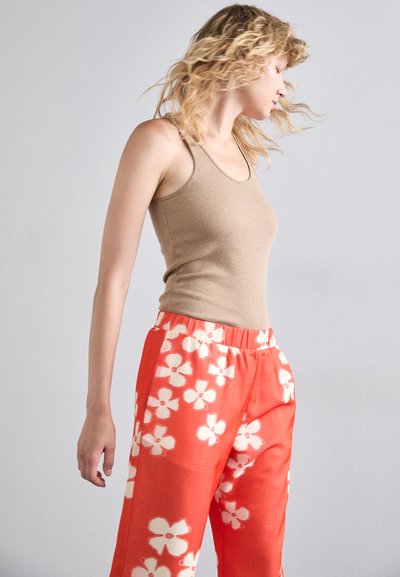Tan fitted tank top and loose orange pants with white floral patterns. The outfit features a stretchy waistband and smooth texture.