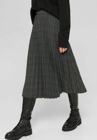 Falda midi plisada en un patrón de cuadro oscuro, con acentos en azul. Fabricada en un tejido ligero. Combinada con botas de combate negras con cordones.
