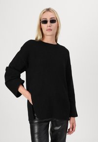 Svart oversized genser med ribbestrikkede mansjetter og nederkant. Har en klassisk rund hals og litt teksturert stoff. Kombinert med svarte skinnbukser.