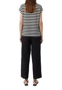 Gestreiftes Kurzarmoberteil in Schwarz und Weiß, kombiniert mit locker sitzenden schwarzen Hosen. Riemchensandalen in Schwarz runden das Outfit ab.