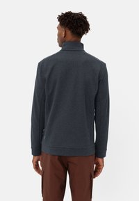 Pullover grigio scuro con colletto alto, tessuto strutturato e maniche lunghe. Presenta un orlo dritto e un sottile accento verde sul lato inferiore.