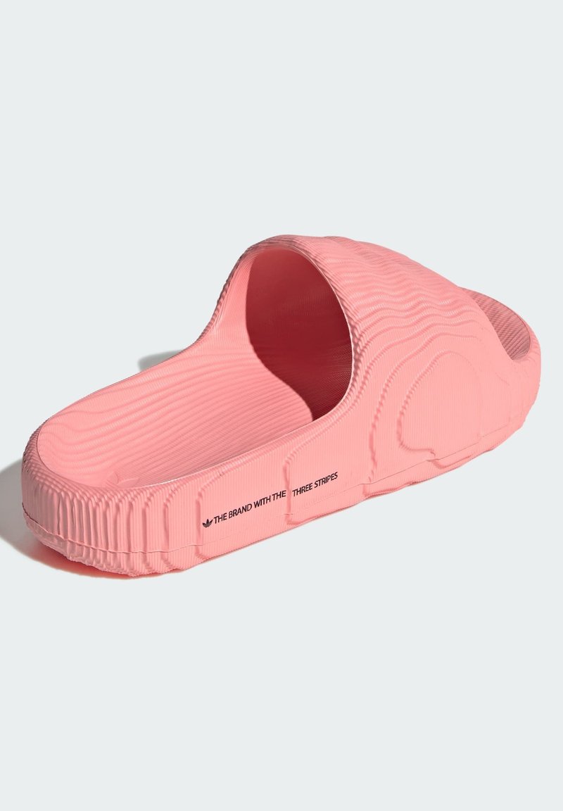 Sandale mule en caoutchouc rose avec un motif de surface ondulé texturé, dos ouvert et semelle surélevée. Présente un logo sur le côté.