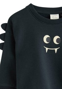 Mørkeblå sweatshirt til småbørn med rund hals, legesyg monsteransigtstryk og stofpigge langs skuldersømmen.