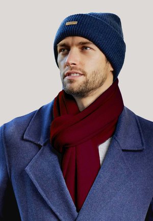 Cappello a maglia blu navy, sciarpa a coste color borgogna e cappotto grigio con colletto a revers. Presenta materiali testurizzati e un design casual.