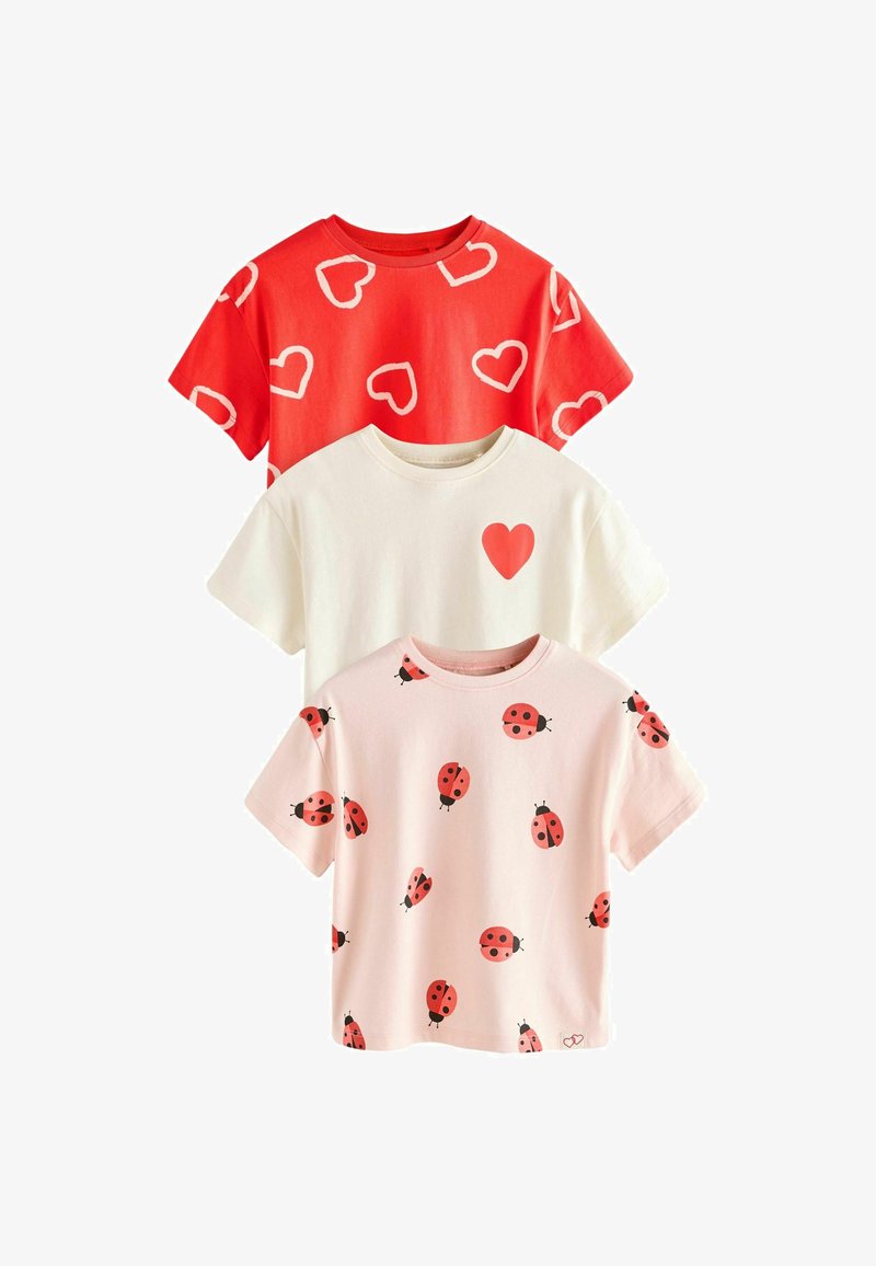 Trois chemises à manches courtes avec col rond : rouge avec des cœurs blancs, blanche avec un cœur rouge sur la poitrine, et rose pâle avec des coccinelles rouges.