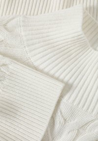 Tessuto di un maglione lavorato a maglia bianco con texture a coste e a treccia, caratterizzato da righe spesse e sottili. Aspetto morbido e accogliente con un design versatile.