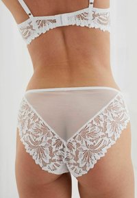 Weißes Spitzen-Unterwäsche-Set mit durchscheinendem Rücken, detaillierter Blumen-Spitzenverzierung und einem weichen Bund. Das Design betont zarte Texturen.