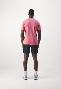 Růžové tričko s krátkým rukávem a kulatým výstřihem spárované s námořnickými kraťasy. Osoba má na sobě bílé ponožky a šedé sportovní boty.