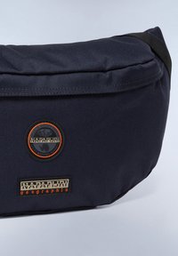 Tmavě modrá nylonová crossbody taška s zakřiveným tvarem, zdobená kulatými logovými nášivkami a texturovaným povrchem. Obsahuje černý popruh a zipy.