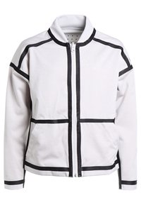 Weiße Jacke mit schwarzen Akzenten, mit einem Reißverschluss vorne, Stehkragen und geometrischen Panelelementen. Hergestellt aus einem glatten, strukturierten Stoff.