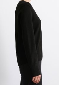 Schwarzer Pullover mit rundem Halsausschnitt, langen Ärmeln sowie gerippten Bündchen an Ärmeln und Saum. Der Stoff wirkt glatt mit einer dezenten Textur.