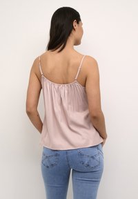 Light pink sleeveless top with gathered back and adjustable straps, paired with fitted light blue jeans featuring back pockets and stitching details.