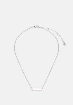 Hõbedane kettkaelakee, millel on ristküliku kujuline ripats, millel on graveeritud logo ja väike ümmargune aksent. Kett on varustatud homaariklambri ja pikendusketiga.