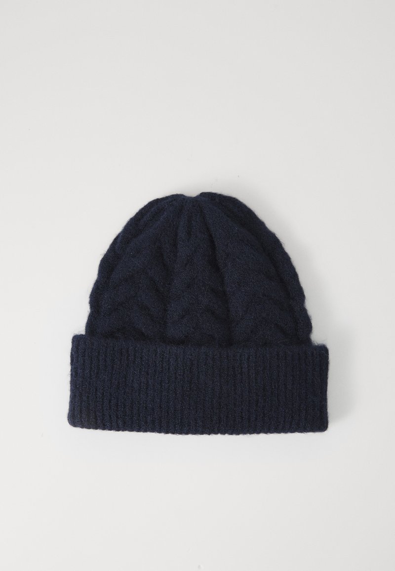 Beanie in lana lavorata a maglia di un blu navy scuro, con risvolto a coste e motivo a treccia, su uno sfondo bianco semplice.