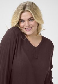 Long-sleeve, deep burgundy top made of lightweight fabric with a V-neck and a small front placket detailing. Soft texture, relaxed fit.