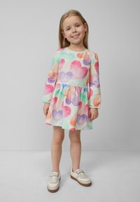 Langärmliges Kleid in Pastellfarben mit Herzmuster, strukturiertem Stoff und gerafftem Taille, kombiniert mit weißen Sneakern.