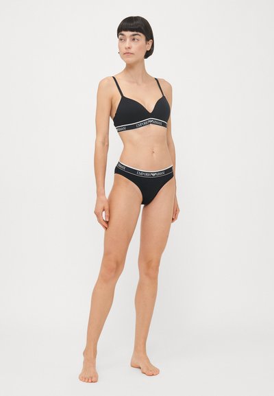 Conjunto de sujetador y bikini negro con diseño de escote en V, tirantes finos y banda elástica de marca con el texto "EMPORIO ARMANI". Textura de tela suave.