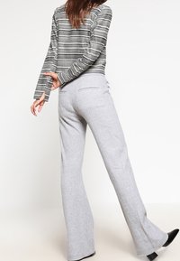 Pantalon évasé gris en tissu doux, avec une texture lisse et deux poches arrière. Le haut est rayé noir et blanc avec des manches longues.