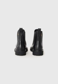 Bottines noires en cuir avec une finition lisse, panneaux latéraux élastiques, languettes de tirage et semelles en caoutchouc texturées pour une bonne adhérence.