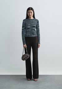 Kék tónusú csíkos hosszú ujjú felső, fekete, cakkos mintás bő szárú nadrág, apró kerek táska láncos fogantyúval, és nyitott orrú cipők.