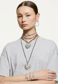 Strieborné šperky zahŕňajú viacvrstvové náhrdelníky s pendantom vo forme pazúra, hrubé retiazky, kruhové náušnice a náramky s rôznymi tvarmi a akcentmi.