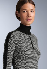 Crno-bijeli pleteni pulover s visokim ovratnikom, s detaljem na zatvaraču i kontrastnim crnim akcentima na ramenima.