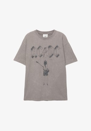 Harmaa puuvillapaita, jossa on suuri AC/DC-logo ja graafinen kuva kitaristista takana, lyhyillä hihoilla ja pyöreällä kaula-aukolla.