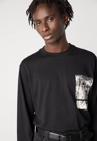 Zwarte longsleeve t-shirt van katoen, voorzien van een zak met een zwart-wit grafisch ontwerp, ronde halslijn en een ontspannen pasvorm.