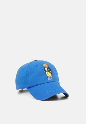 Blaues Baseballcap mit einem gestickten Bären, der eine Jacke, ein gestreiftes Hemd, gelbe Hosen trägt und darunter den Schriftzug "POLO".