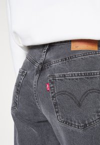 Jeans in denim grigio con un classico design a cinque tasche. Presentano un'etichetta rossa Levi's e un motivo distintivo di cucitura sulla tasca posteriore.