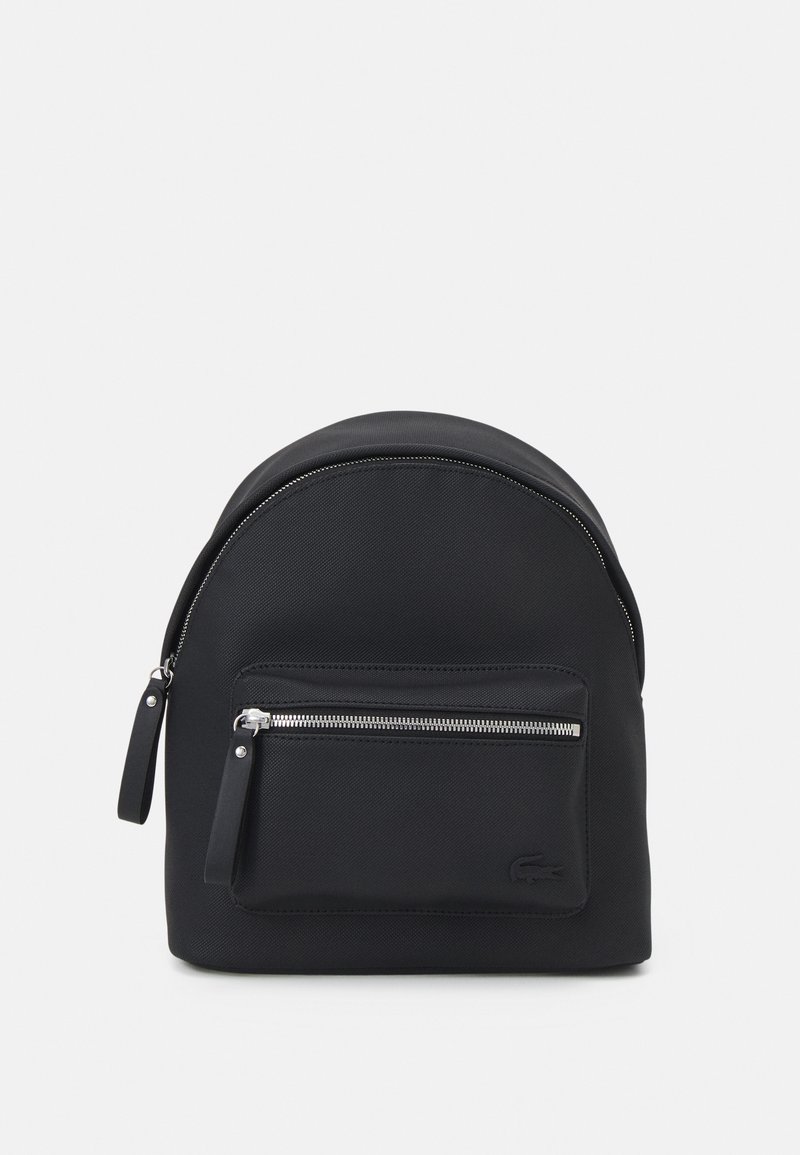 Sac à dos compact noir avec une poche zippée à l'avant et des tirettes de zip en argent, présentant un logo en relief discret dans le coin inférieur droit.